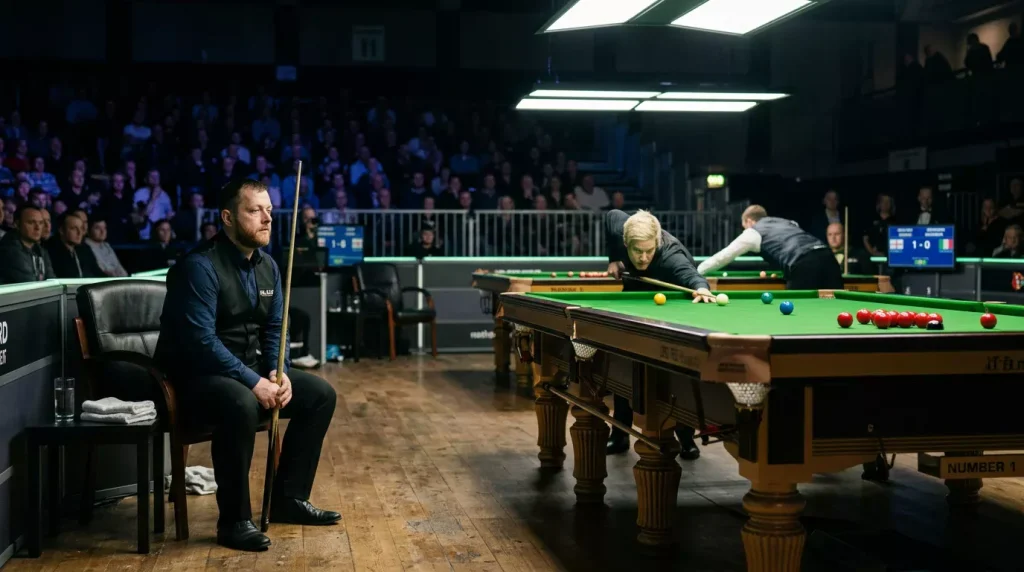 Snookerspeler kijkt toe vanaf zijn stoel terwijl de tegenstander aan de tafel speelt
